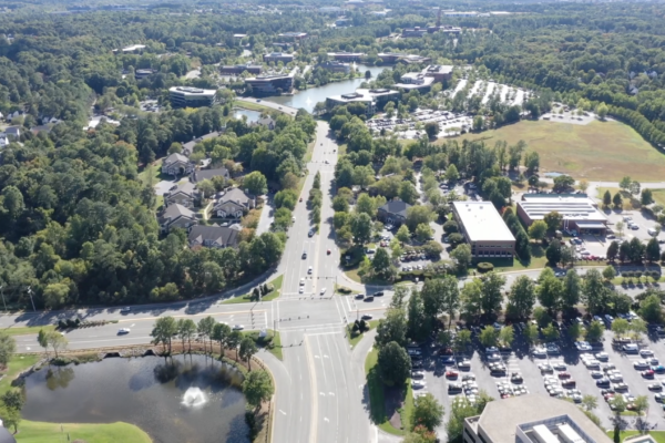 Aerial view: suburb with roads, buildings, pond, and trees.